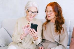 Bild von zwei älteren Frauen die lächeln, während sie ein Smartphone benutzen